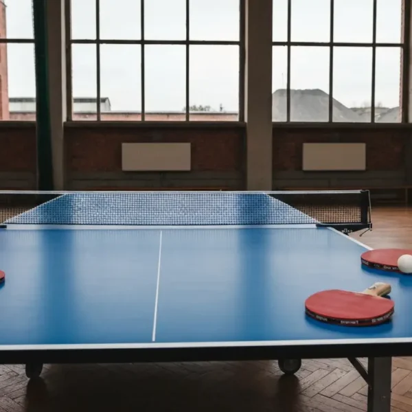 Stol do tenisa stolowego z czterema paletkami i pileczka przy linii srodkowej w slaskiej hali sportowej